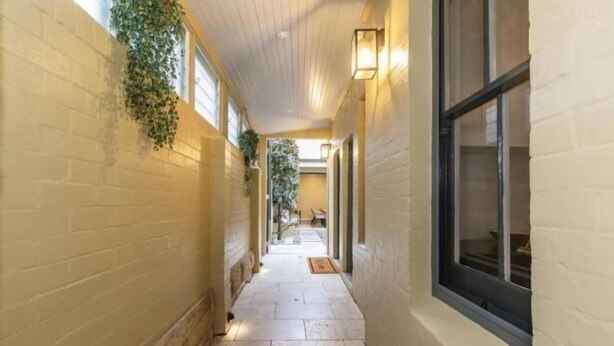A narrow hallway with brick walls, a tiled floor, and a window on the right. - Millers Point Home Harbourside (Millers Point)