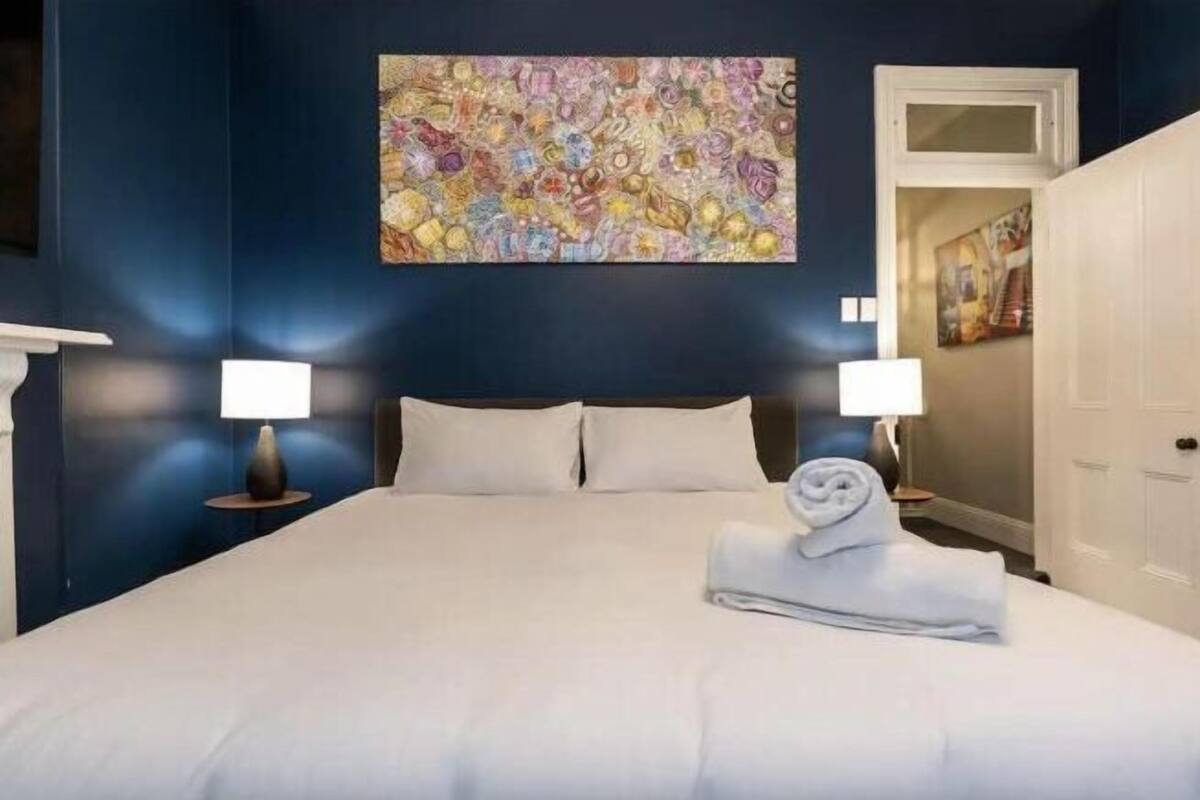 Une chambre d’hôtel avec un grand lit, deux lampes de chevet, un tableau au mur et une porte donnant sur une autre pièce.