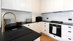 A modern kitchen with white cabinetry, a black countertop, a stainless steel sink, a gas stove, and a microwave. - Millers Point Home Harbourside (Millers Point)