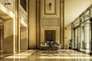 A lobby with a patterned floor, a sofa with decorative pillows, and a large mirror above a door.