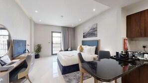 A modern hotel room with a bed, desk, chair, and kitchenette. - Suha Al Jaddaf (Dubai)