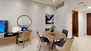 A modern dining area with a round wooden table, four chairs, a laptop, a television, and a decorative plant. - Suha Al Jaddaf (Dubai)