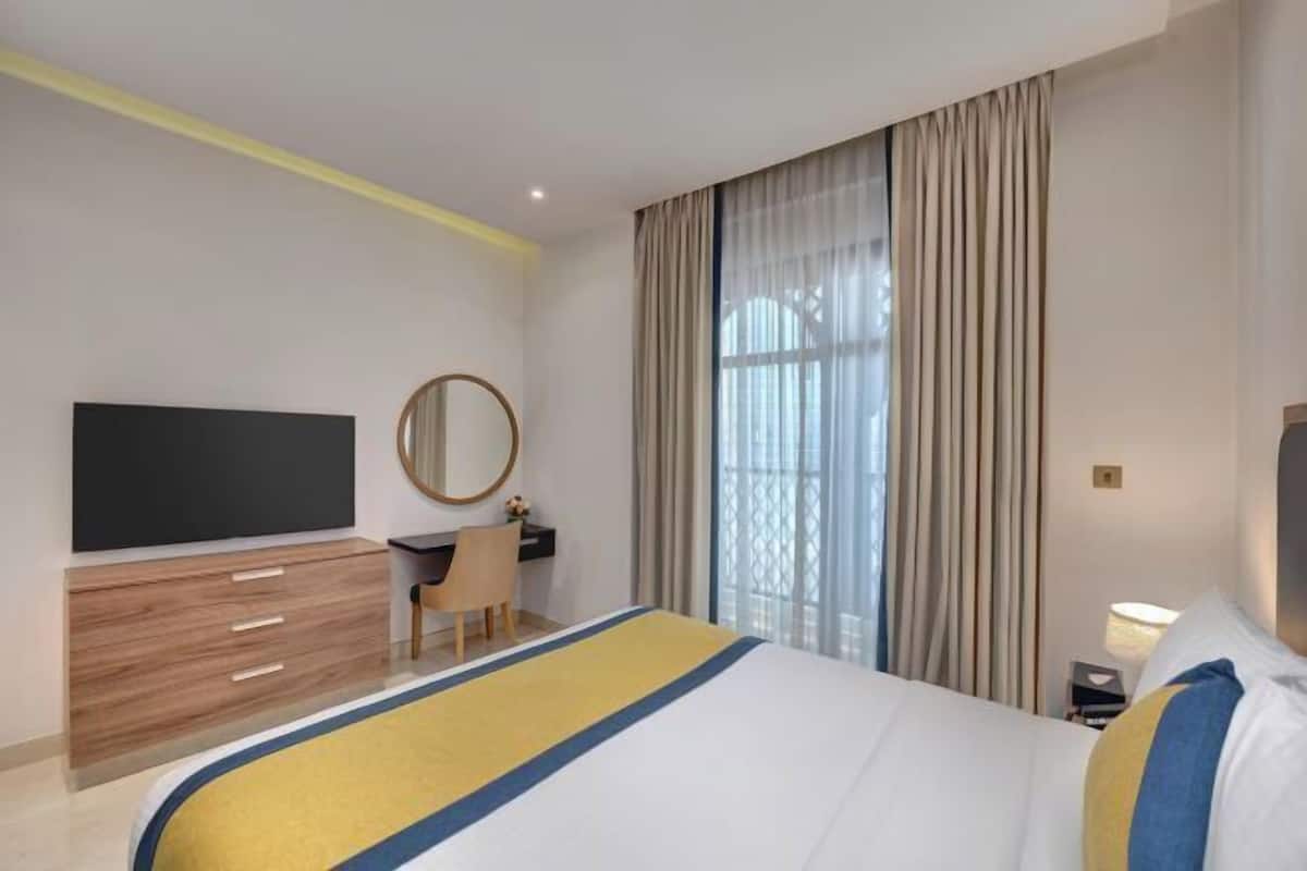 Une chambre d’hôtel équipée d’un lit, d’un bureau, d’une chaise, d’une télévision et d’une grande fenêtre avec des rideaux.