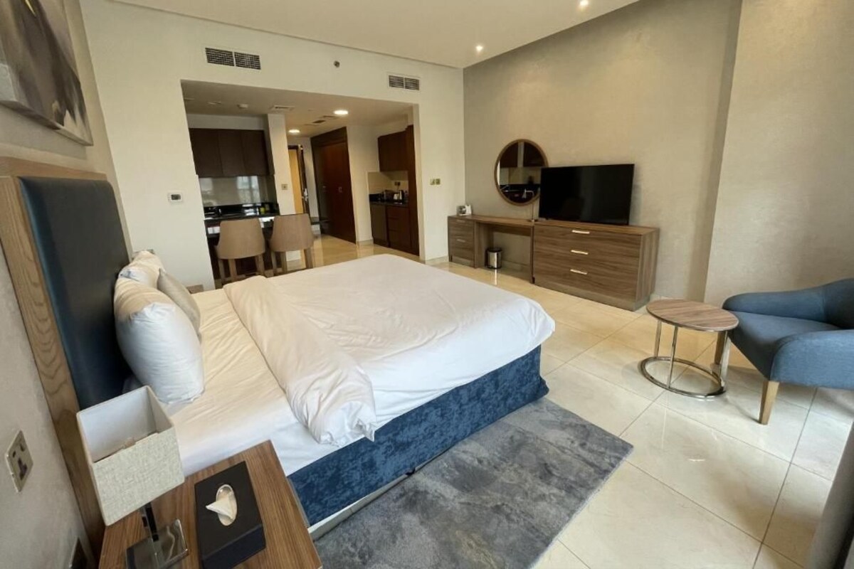 A modern hotel room with a large bed, a TV, a desk, and a seating area.