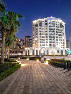 A multi-story hotel with a prominent star sign on the roof, a paved walkway, and palm trees. - Suha Al Jaddaf (Dubai)