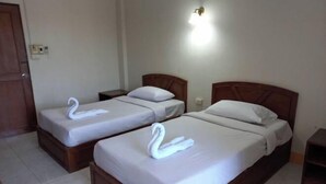 Camera d'albergo con due letti, ciascuno con copripiumino bianco e un asciugamano a forma di cigno. Tra i letti si trova un comodino con una lampada.