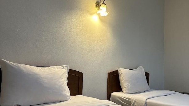 Due letti singoli con testiere in legno e biancheria da letto bianca, una lampada a parete e una parete semplice.