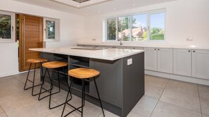 Eine moderne Küche mit einer zentralen Kochinsel, Barhocker und großen Fenstern.