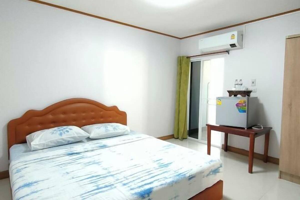 A bedroom with a bed, a TV on a stand, and an air conditioning unit.
