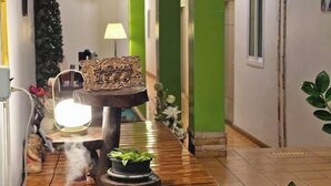 A hallway with a wooden table, a decorative sign, a lamp, and a plant. - Khunnampheung Apartment (Sakon Nakhon)