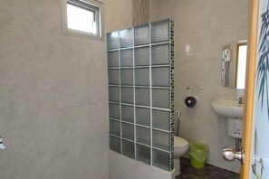 A bathroom with a toilet, a sink, a green trash bin, and a window. - Khunnampheung Apartment (Sakon Nakhon)