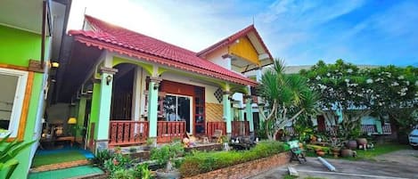 A two-story house with a red roof, a porch, and a garden.