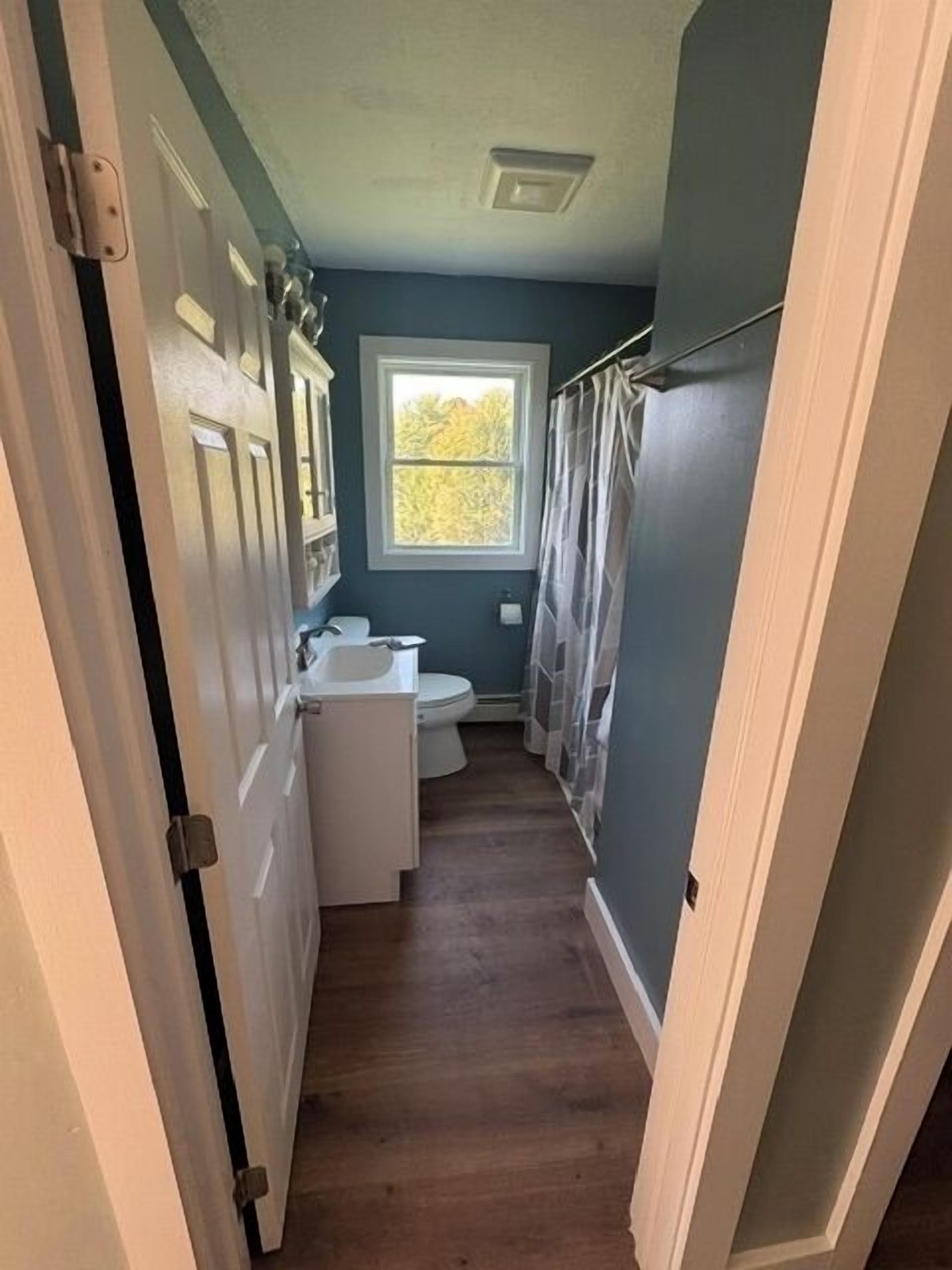 A narrow bathroom with a toilet, sink, and window.