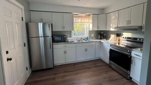 Una cucina con mobili bianchi, elettrodomestici in acciaio inossidabile, una finestra con tende e pavimento in legno.