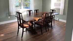 Una sala da pranzo con tavolo e sedie in legno, ampie finestre con tende e una lampada a sospensione.