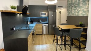 Een moderne keuken met een ingebouwde oven, magnetron en koelkast. Er is een houten eettafel met twee stoelen en een kleine plant in een pot op het aanrecht.