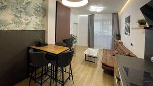 Een moderne woonkamer met een houten salontafel, een bruine bank en een eethoek met een houten tafel en zwarte stoelen.