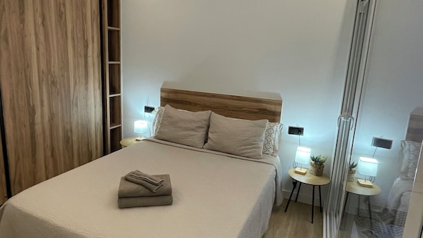 Een moderne slaapkamer met een groot bed, een houten hoofdbord, nachtkastjes met lampen en een schuifdeur van glas.