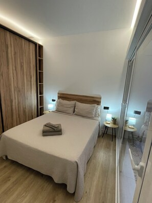 Une chambre moderne avec un grand lit, une tête de lit en bois, des tables de chevet avec des lampes et une porte-fenêtre coulissante.