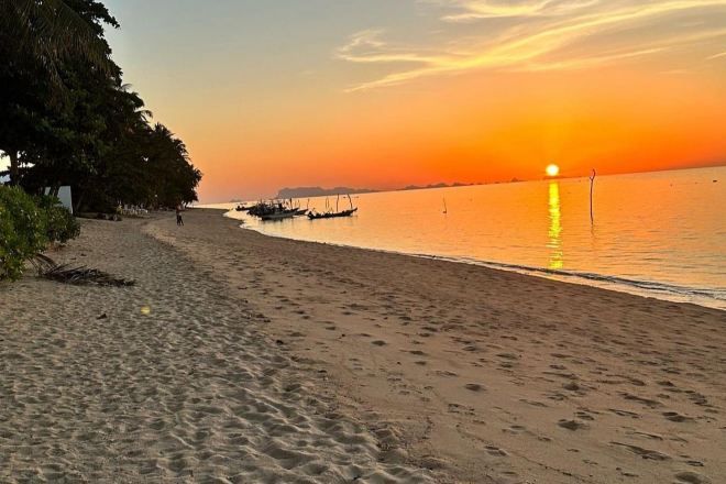 Una playa con barcos, cielo despejado y una puesta de sol.