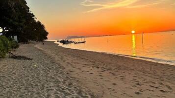 Una playa con barcos, cielo despejado y una puesta de sol.