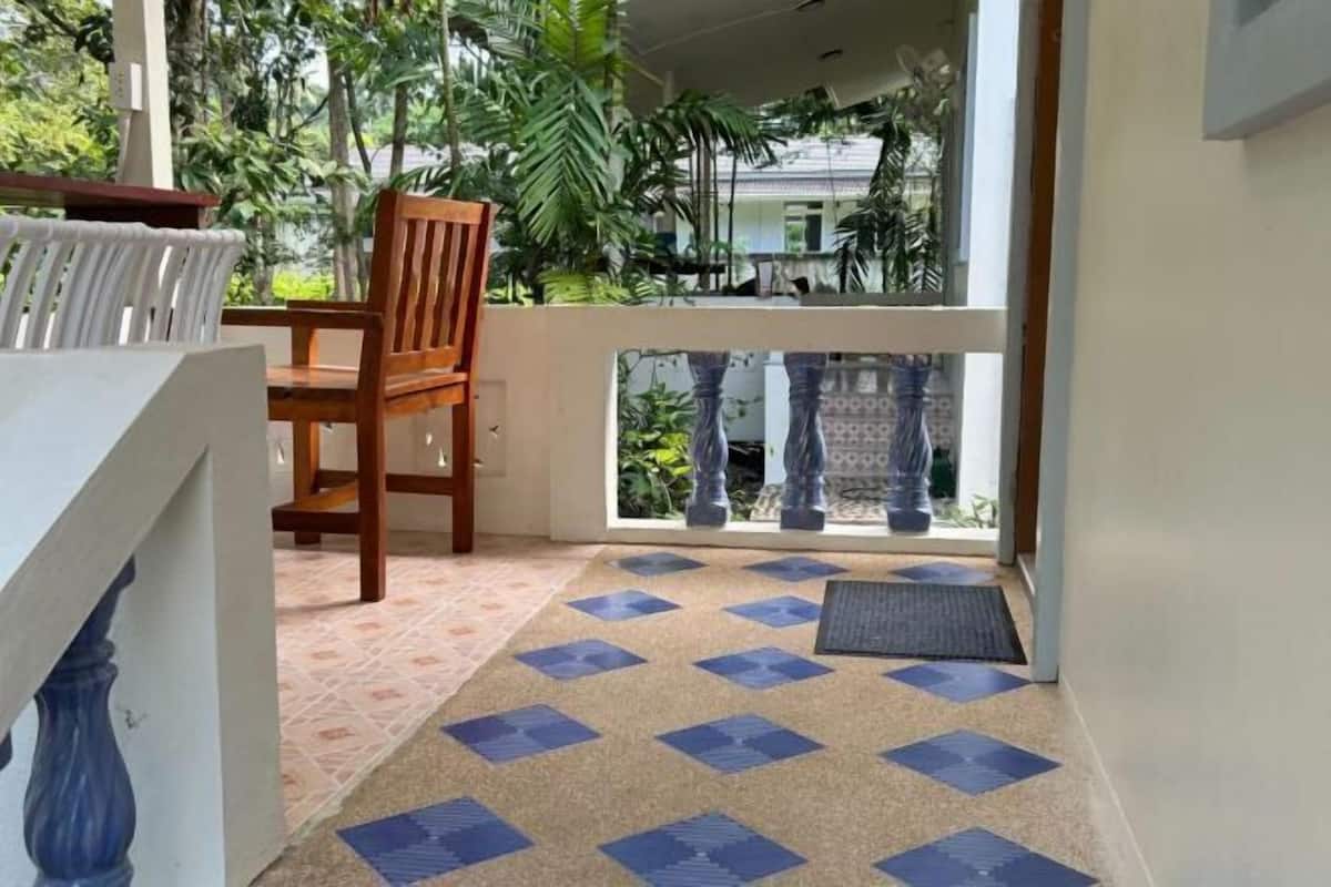 Un balcón con piso estampado, una silla de madera y vistas a zonas verdes y edificios.