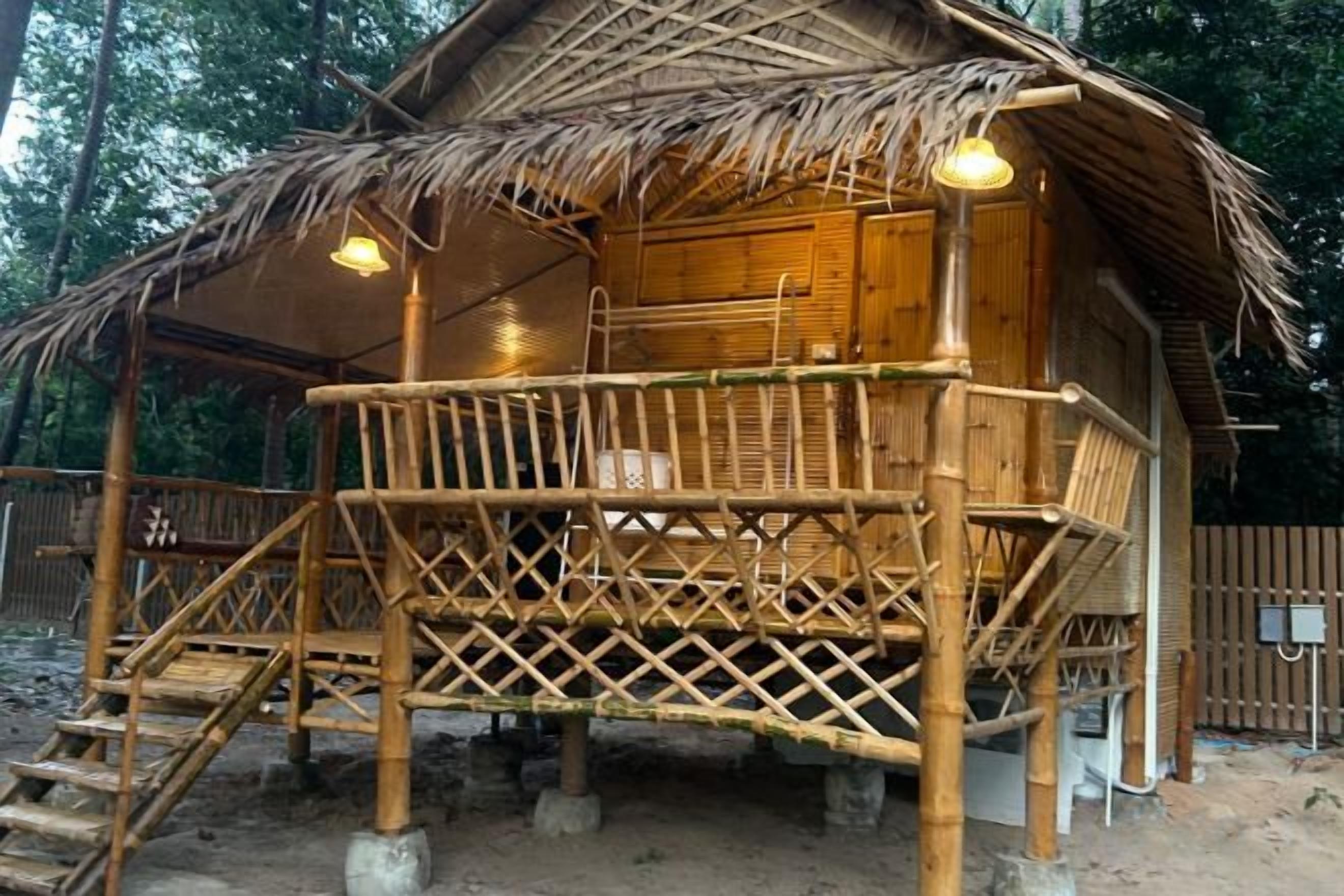 Estructura de bambú con techo de paja, terraza de madera y escalera que lleva a la entrada.
