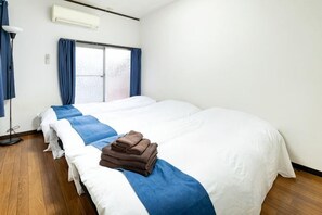A hotel room with two beds, a window with curtains, and an air conditioning unit. - 8 min by train from Ikebukuro Station, 18 min from Shinjuku Station (Tokyo)