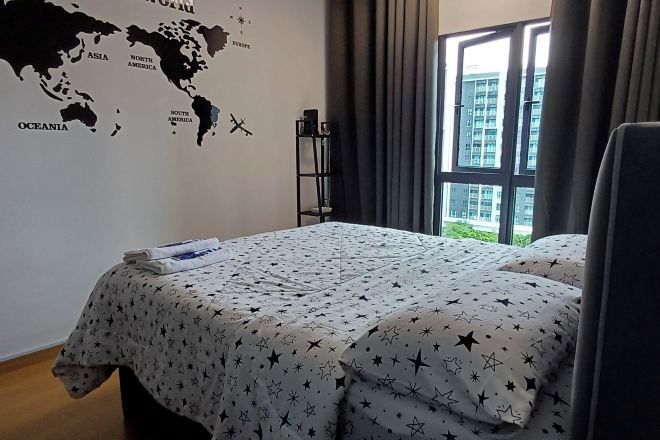 A hotel room with a bed, a world map wall decoration, a window with curtains, and a view of buildings outside.