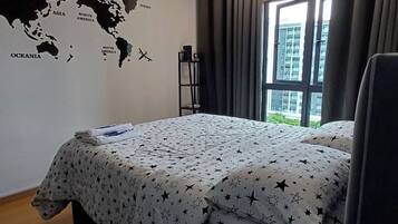 A hotel room with a bed, a world map wall decoration, a window with curtains, and a view of buildings outside.