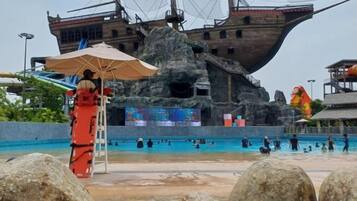 Una gran piscina exterior con un decorado con temática náutica, un puesto de socorrista y grandes rocas al frente.