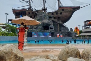 Een groot buitenzwembad met een achtergrond in scheepsdecor, een badmeesterstand en grote rotsen op de voorgrond.