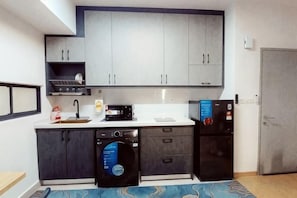 A compact kitchen with grey cabinets, a dishwasher, a microwave, and a refrigerator.