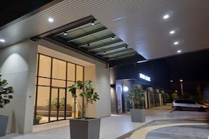 Entrada de hotel con puerta de vidrio, plantas en macetas y un cartel sobre la puerta.