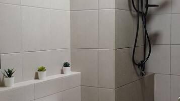 A bathroom with white tiles, a toilet, a shower area, and small potted plants on the wall.