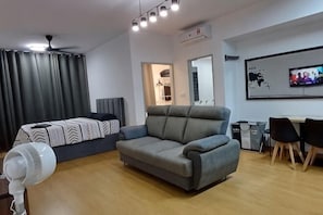 A modern living room with a sofa, a bed, a dining area, and a TV. - LuuMa@Gamuda Cove (Tanjung Dua Belas)