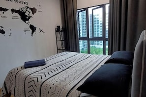 Ein Hotelzimmer mit einem Bett, einer Weltkarte an der Wand, einem Fenster mit VorhÀngen und Blick auf GebÀude.