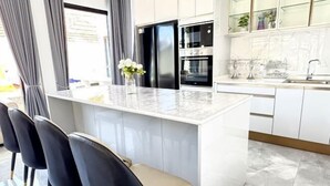 A modern kitchen with a marble island, black appliances, and a view of the street. - The White House Pool Villa Pattaya (Pattaya)