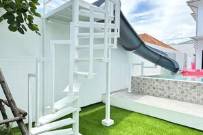 A white outdoor play structure with a slide, a small pool with a tiled deck, and artificial grass. - The White House Pool Villa Pattaya (Pattaya)