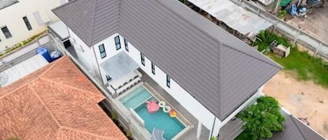 A two-story house with a swimming pool, a slide, and a red-roofed structure.