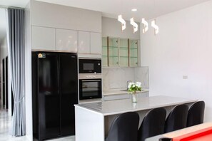 A modern kitchen with a refrigerator, oven, microwave, and a dining area with chairs. - The White House Pool Villa Pattaya (Pattaya)