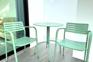 Two green metal chairs and a small round table on a balcony with a glass partition. - The White House Pool Villa Pattaya (Pattaya)