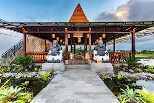 Un restaurante con entrada cubierta, dos estatuas de piedra y un estanque con plantas tropicales.