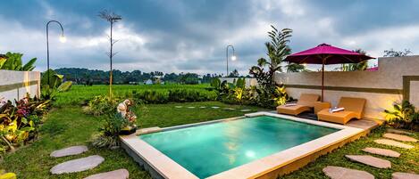 A rectangular pool with a stone border, surrounded by a well-maintained lawn and stepping stones.