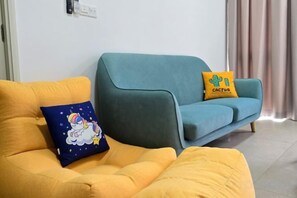 A living room with a yellow sofa and a teal sofa, each with a decorative pillow. - 2BR@Afiniti(8PAX) 3mins Walk to Legoland (Iskandar Puteri)