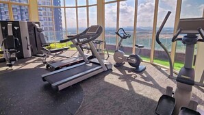 A gym with cardio equipment and a view of a cityscape through large windows. - 2BR@Afiniti(8PAX) 3mins Walk to Legoland (Iskandar Puteri)