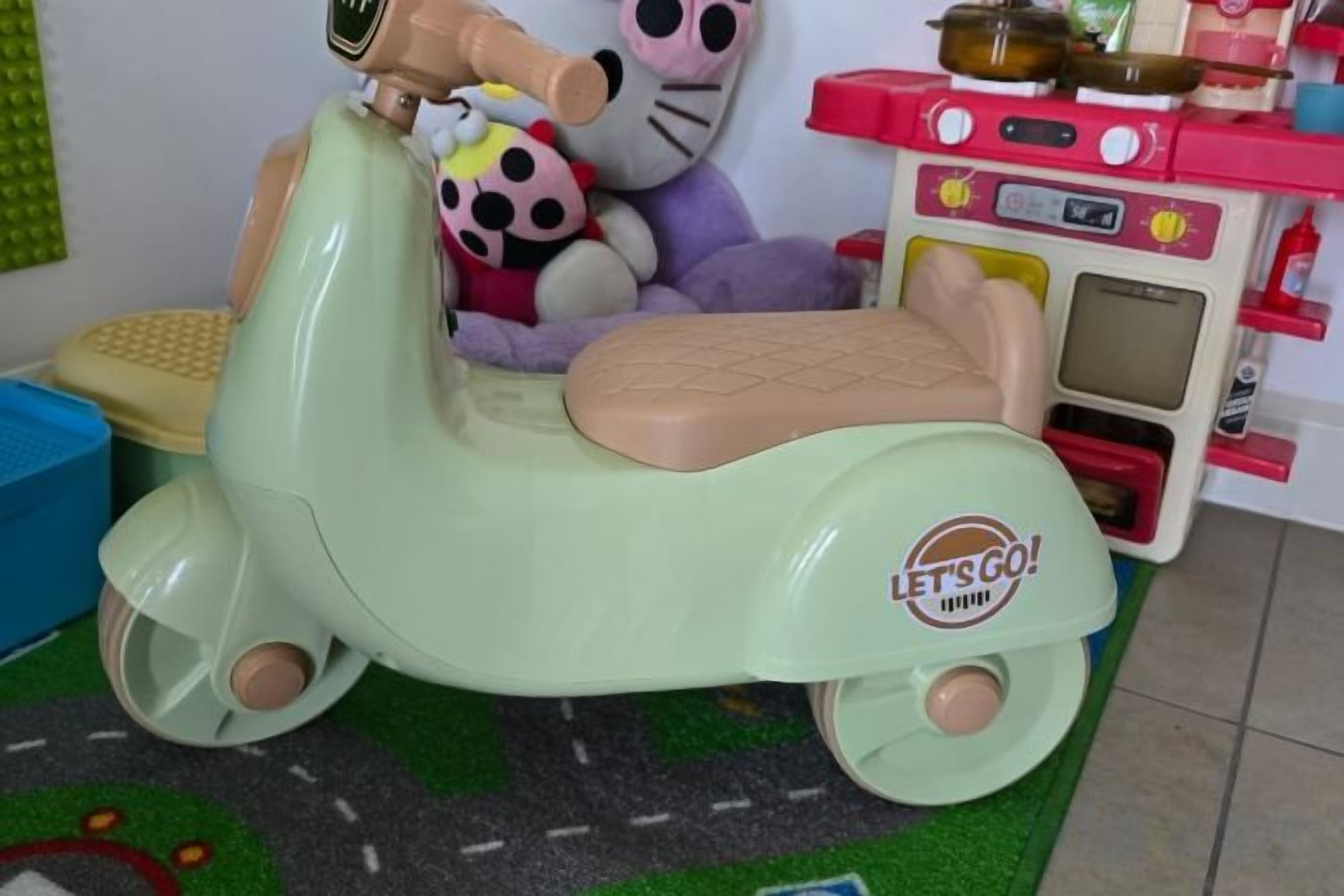 A children's toy scooter with a 'Let's Go!' sticker, a toy kitchen set, and a plush toy in the background.