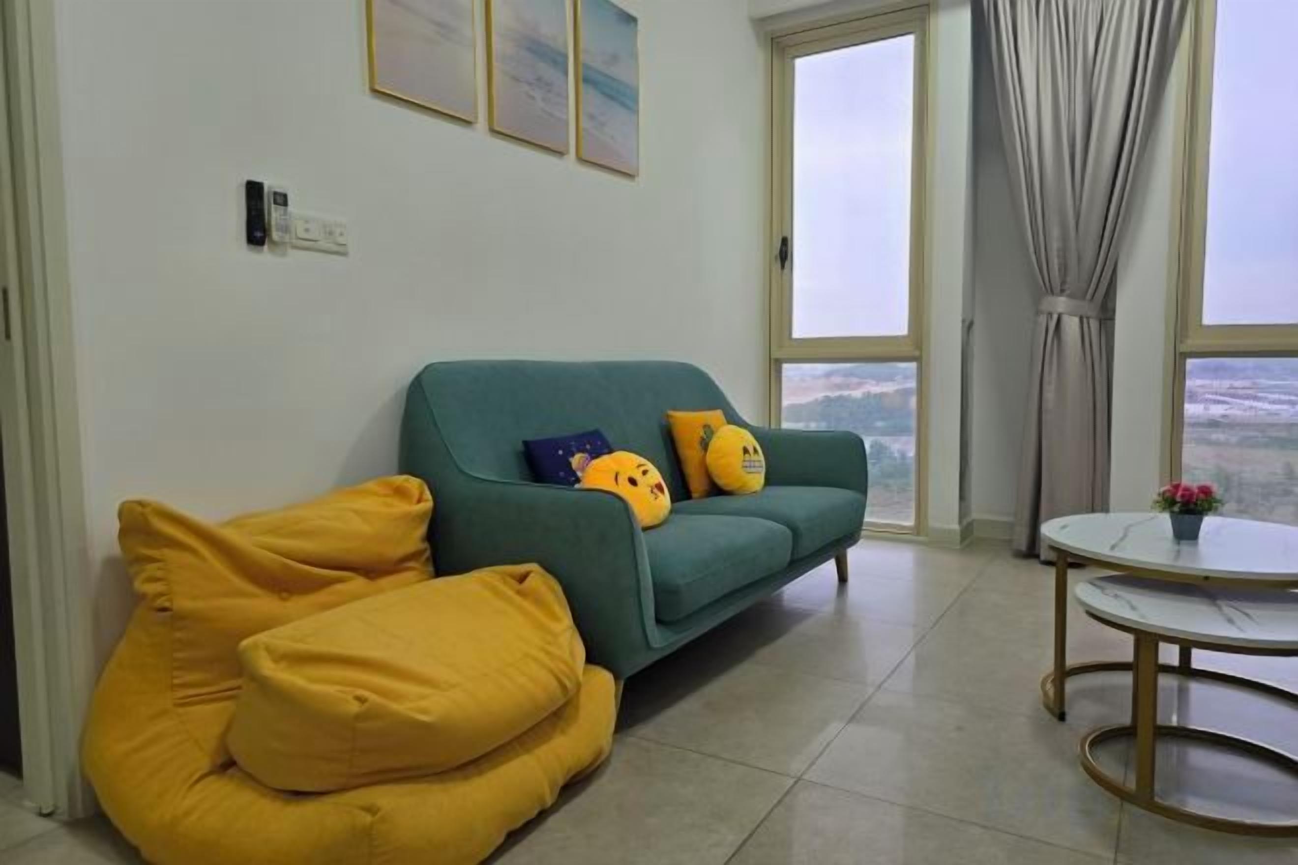 Una sala de estar con sofá, cojines amarillos, una mesa redonda con una flor y vistas amplias a través de grandes ventanas.
