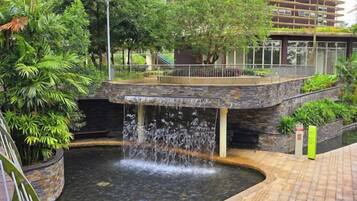 A water feature with a waterfall, surrounded by greenery and a stone structure.