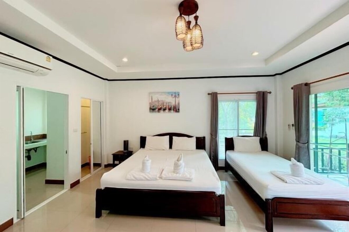 A hotel room with a large bed, a smaller bed, a bedside table, a nightstand, a window with curtains, and a painting on the wall.